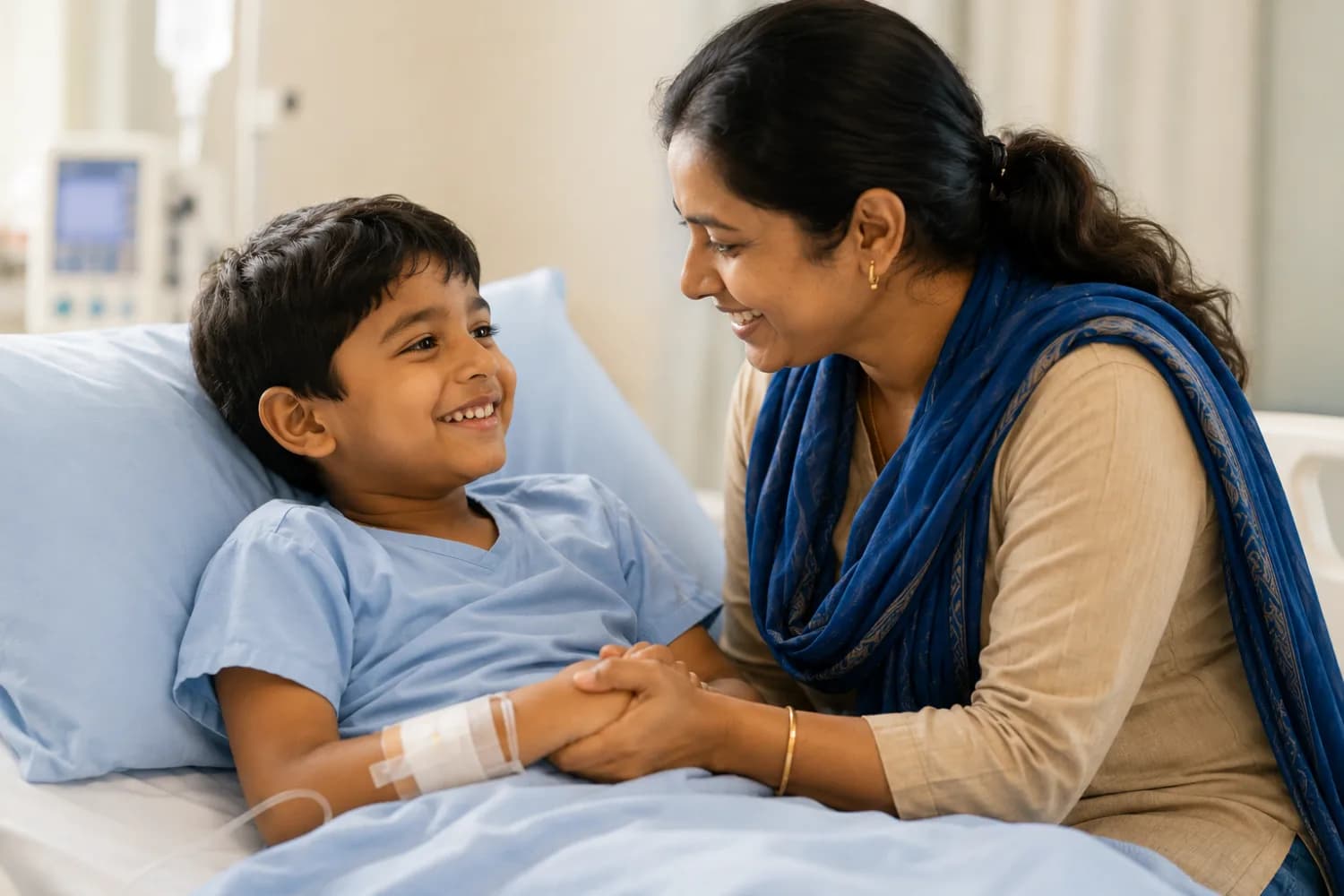 A boy recovering in a hospital bed shares a smile with his mother, who holds his hand.